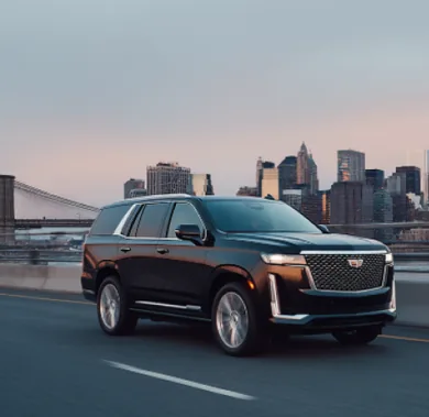 A black Cadillac Escalade on a bridge approach with the Manhattan skyline behind it at dusk