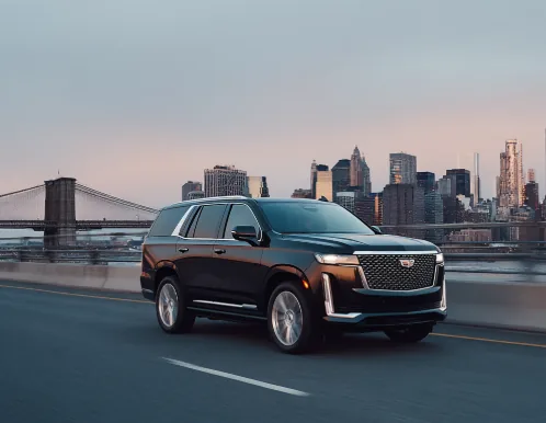 A black Cadillac Escalade on a bridge approach with the Manhattan skyline behind it at dusk