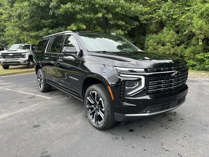 A black Chevrolet Suburban executive SUV seen from the front three-quarter angle, with trees behind it